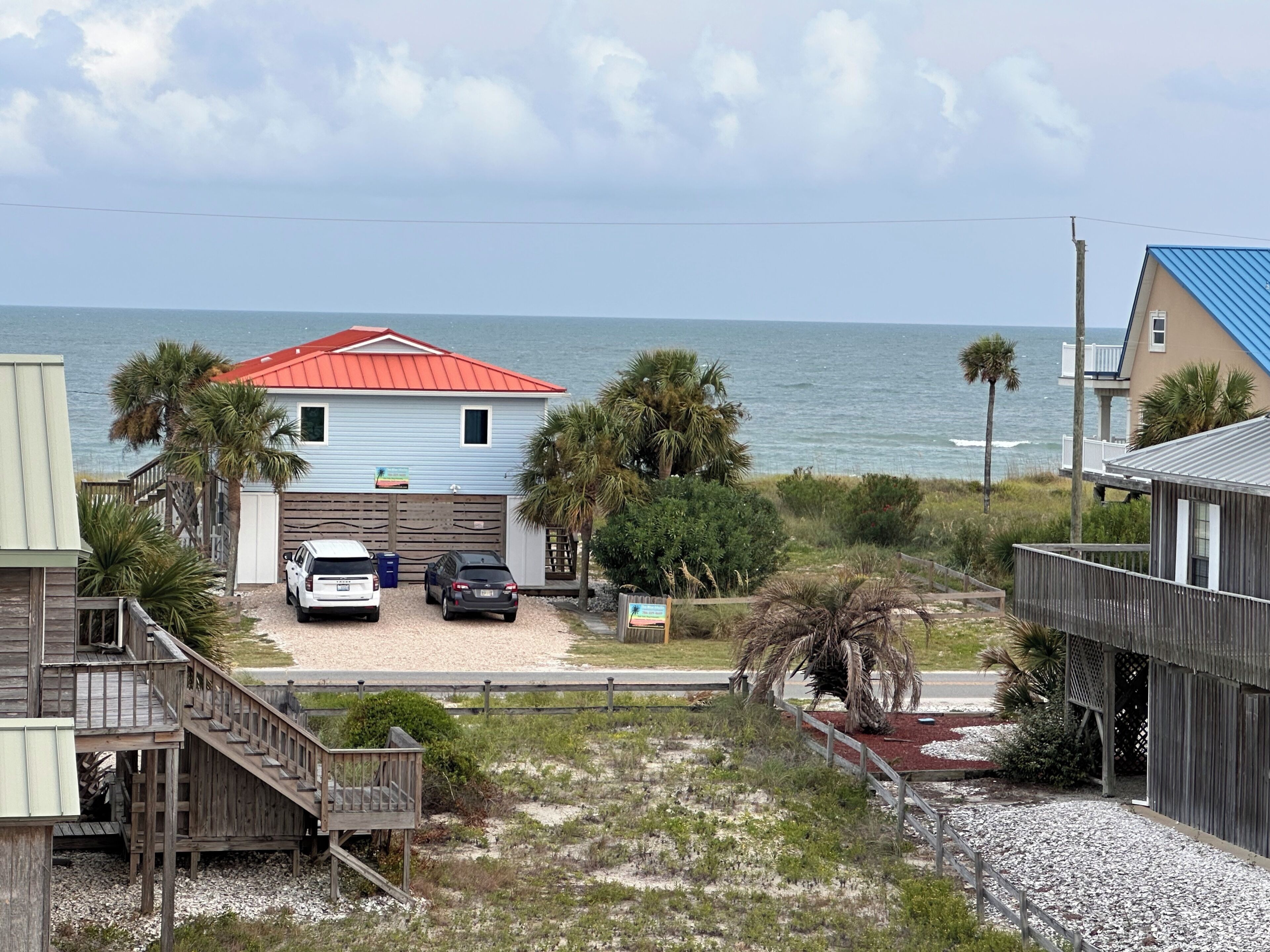 A beachfront property with a two-story house, a covered porch, and a view of the ocean.
