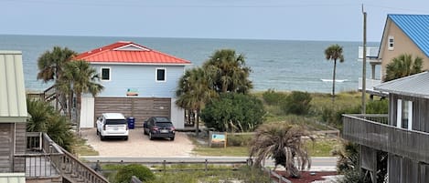 A beachfront property with a two-story house, a covered porch, and a view of the ocean.