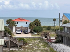 A beachfront property with a two-story house, a covered porch, and a view of the ocean.