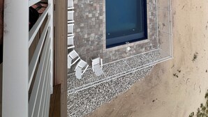 An aerial view of a swimming pool with a surrounding deck, a fenced area, and a building with a balcony.
