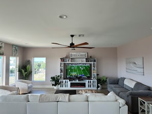 A living room with a television, sofas, a ceiling fan, and a fireplace.