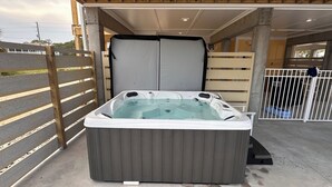 A hot tub in an outdoor covered area with a wooden ceiling and a concrete floor.