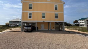 A two-story building with a covered parking area and a gravel driveway.