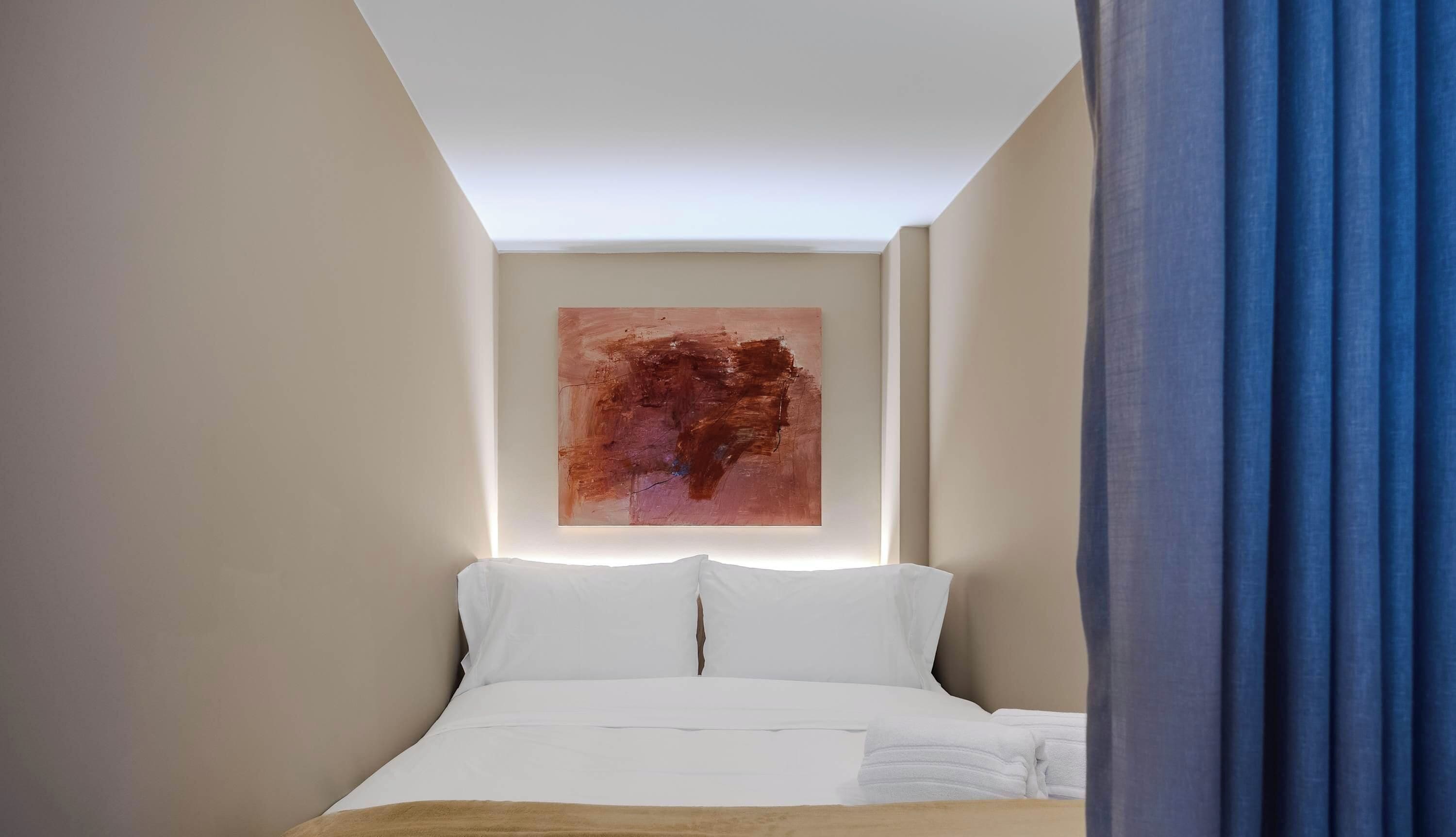 Ein Hotelzimmer mit einem Bett, einem großen abstrakten Gemälde an der Wand und einem blauen Vorhang.