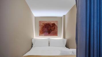 A hotel room with a bed, a large abstract painting on the wall, and a blue curtain.