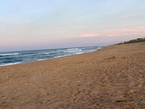 Ein Strand mit sanft abfallendem Hang zum Meer, einem klaren Himmel und einigen Gebäuden in der Ferne.