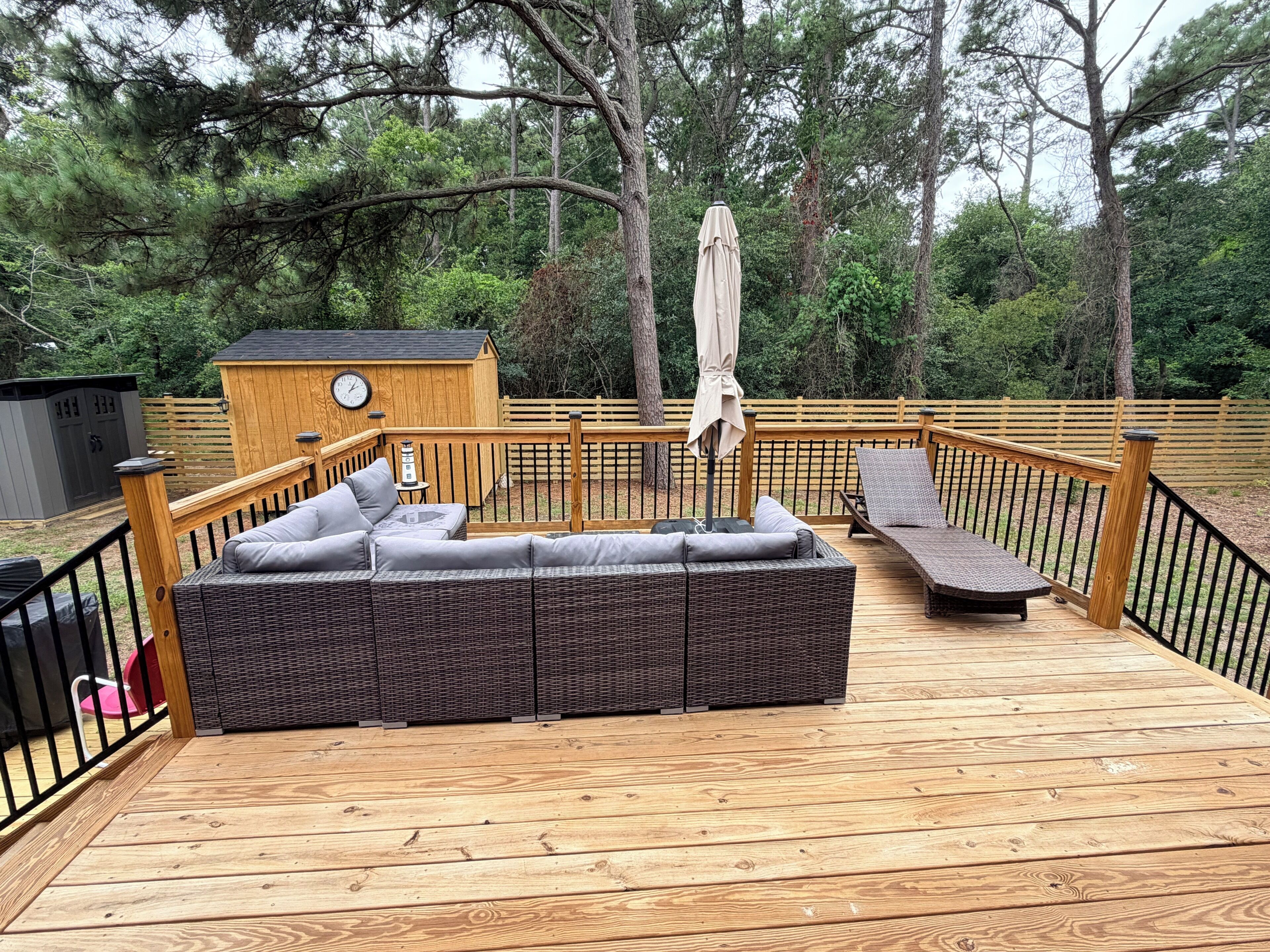 A wooden deck with a wicker sofa and a lounge chair.