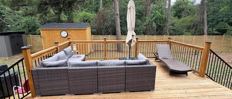 A wooden deck with a wicker sofa and a lounge chair.