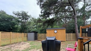 A backyard with a wooden deck, a covered grill, a red chair, and a shed. - Beach Wolf: ALL NEW, impeccable house in Southern Shores, 5 minute walk to beach (Kitty Hawk)