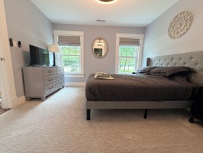 Ein Schlafzimmer mit Bett, Kommode, Fernseher und zwei Fenstern.