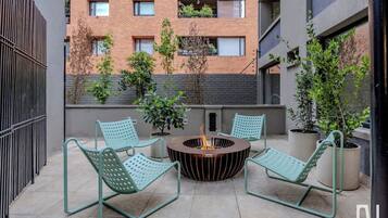 Une terrasse sur le toit avec deux chaises en métal vert, un foyer central et des plantes en pot.