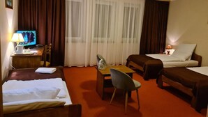 Habitación de hotel con dos camas, un escritorio con silla, televisor y ventana con cortinas.