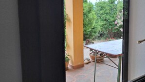 A view through a doorway to an outdoor patio area with a table and chairs, surrounded by greenery and a clear sky. - Casa Rurale - S'Olivare di Filieri (Dorgali)
