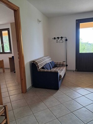 Ein Zimmer mit einer Couch, einer Stehlampe, einer Tür und einem Fenster.