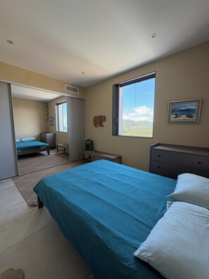 A bedroom with a bed, a desk, a chair, a radiator, and a window with a view. - Vacation Home for Rent (Belgodère)