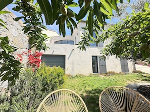 Ein modernes Haus mit Steinwand, Rasen und zwei Korbstühlen.