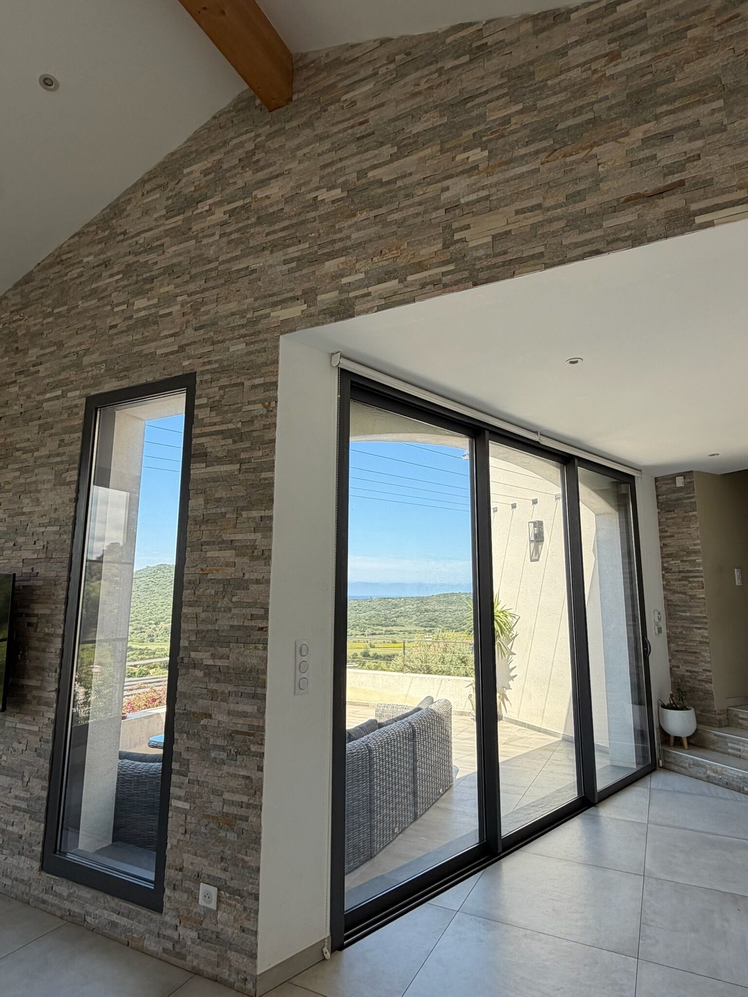 A modern interior with stone wall accents, a large sliding glass door leading to an outdoor patio, and a flat-screen TV mounted on the wall.