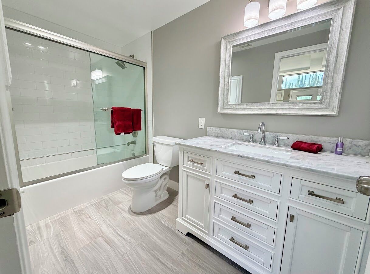 A bathroom with a glass shower enclosure, a white toilet, a white vanity with drawers, and a large mirror above the sink.