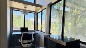 A room with a desk, chair, television, and large windows offering a view of trees and mountains. - Peaceful Foothill Getaway Tennis & 40+ Fruit Trees (Upland)
