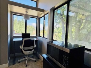 Une chambre équipée d’un bureau, d’une chaise, d’une télévision et de grandes fenêtres donnant sur un paysage de arbres et de montagnes.