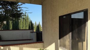 A covered outdoor area with a window, a brick planter with plants, and a view of trees and a fence. - Peaceful Foothill Getaway Tennis & 40+ Fruit Trees (Upland)