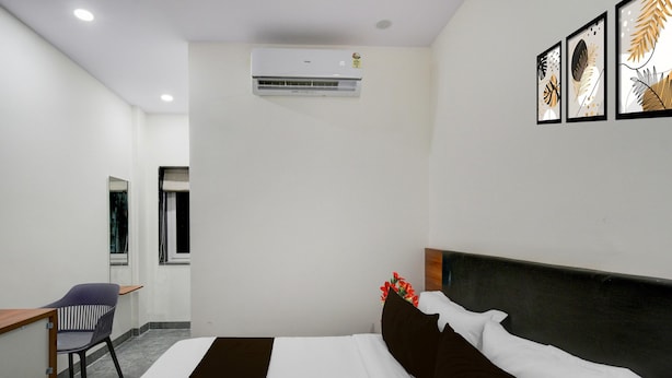 Una habitación de hotel con cama, escritorio, silla, aire acondicionado y obras de arte en la pared.