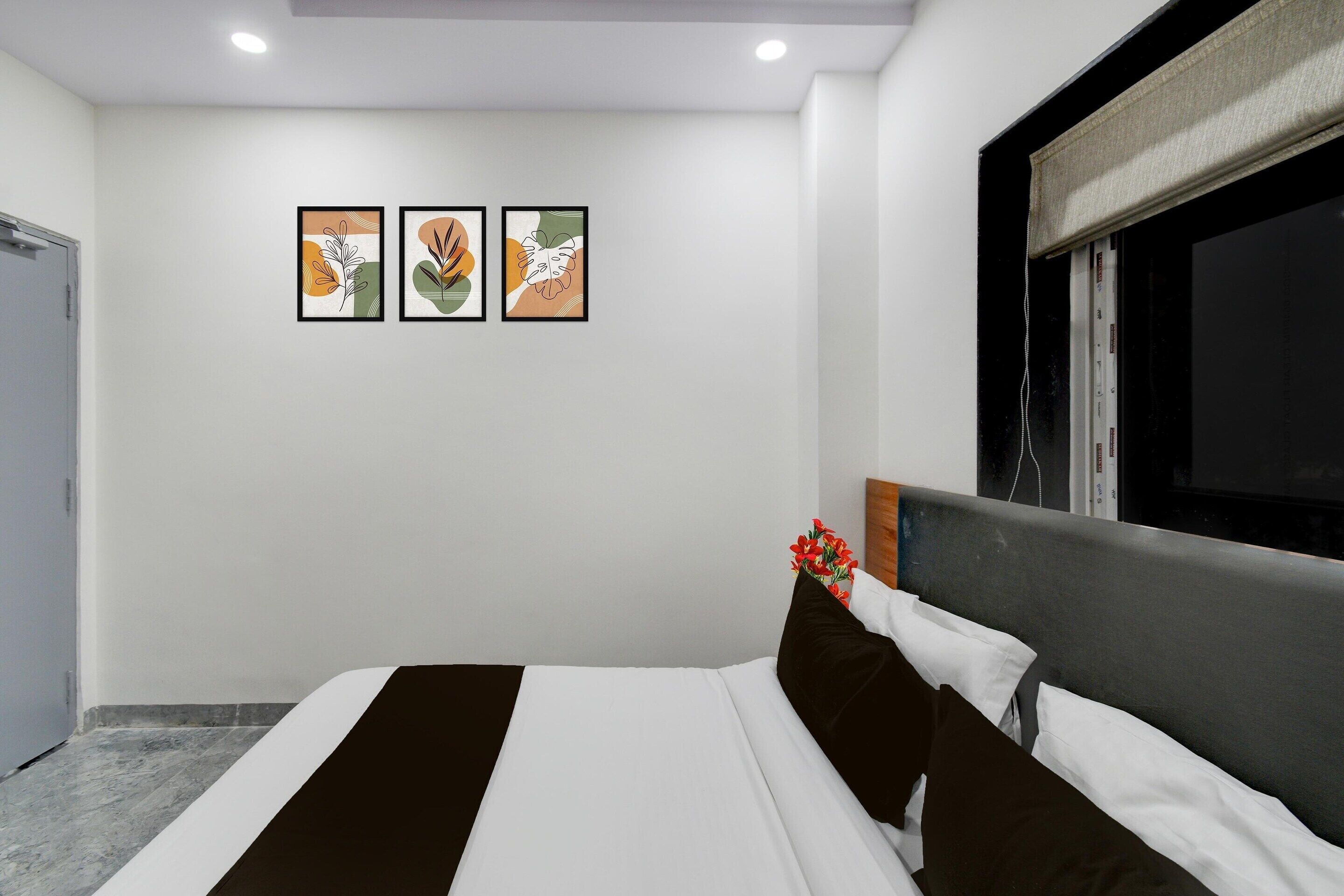 A hotel room with a bed, a window with a blind, and three framed artworks on the wall.