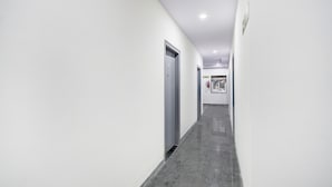 Un pasillo con paredes blancas, suelo gris y una puerta al final.