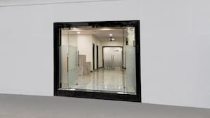 Un pasillo con pared de vidrio, ventilador de techo y piso de mármol.