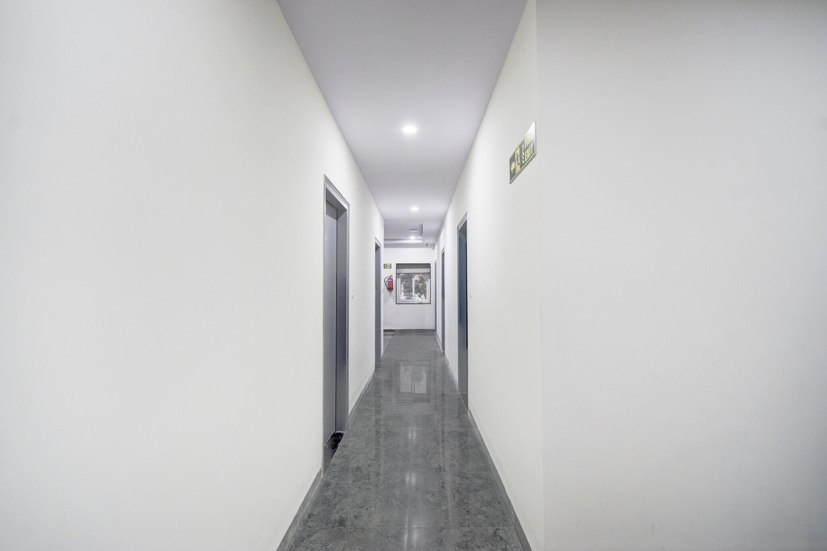 A long, narrow hallway with white walls and a grey floor, leading to a door at the end.