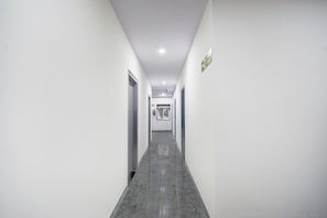 Un pasillo largo y estrecho con paredes blancas y suelo gris, que conduce a una puerta al final.