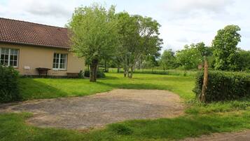 Een huis met pannendak, een grindpad en een gazon met bomen.