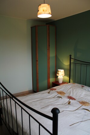 Ein Schlafzimmer mit Bett, Nachttisch, Lampe, Kleiderschrank und einer Treppe.