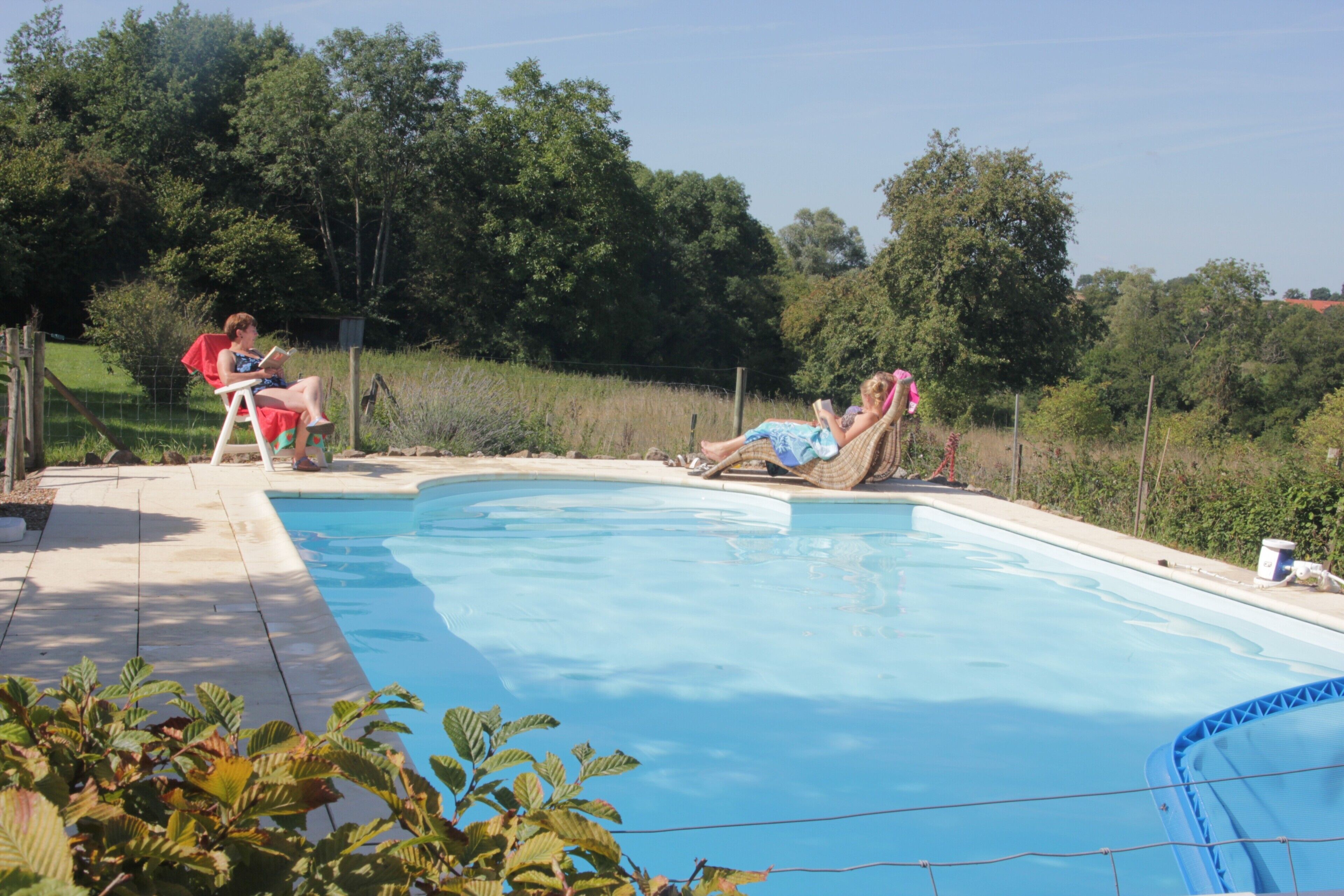 A swimming pool with two lounge chairs and a person reading.