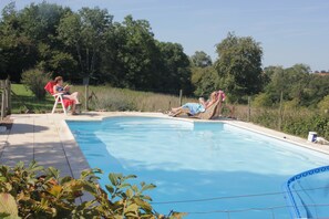 En pool med två solstolar och en person som läser.