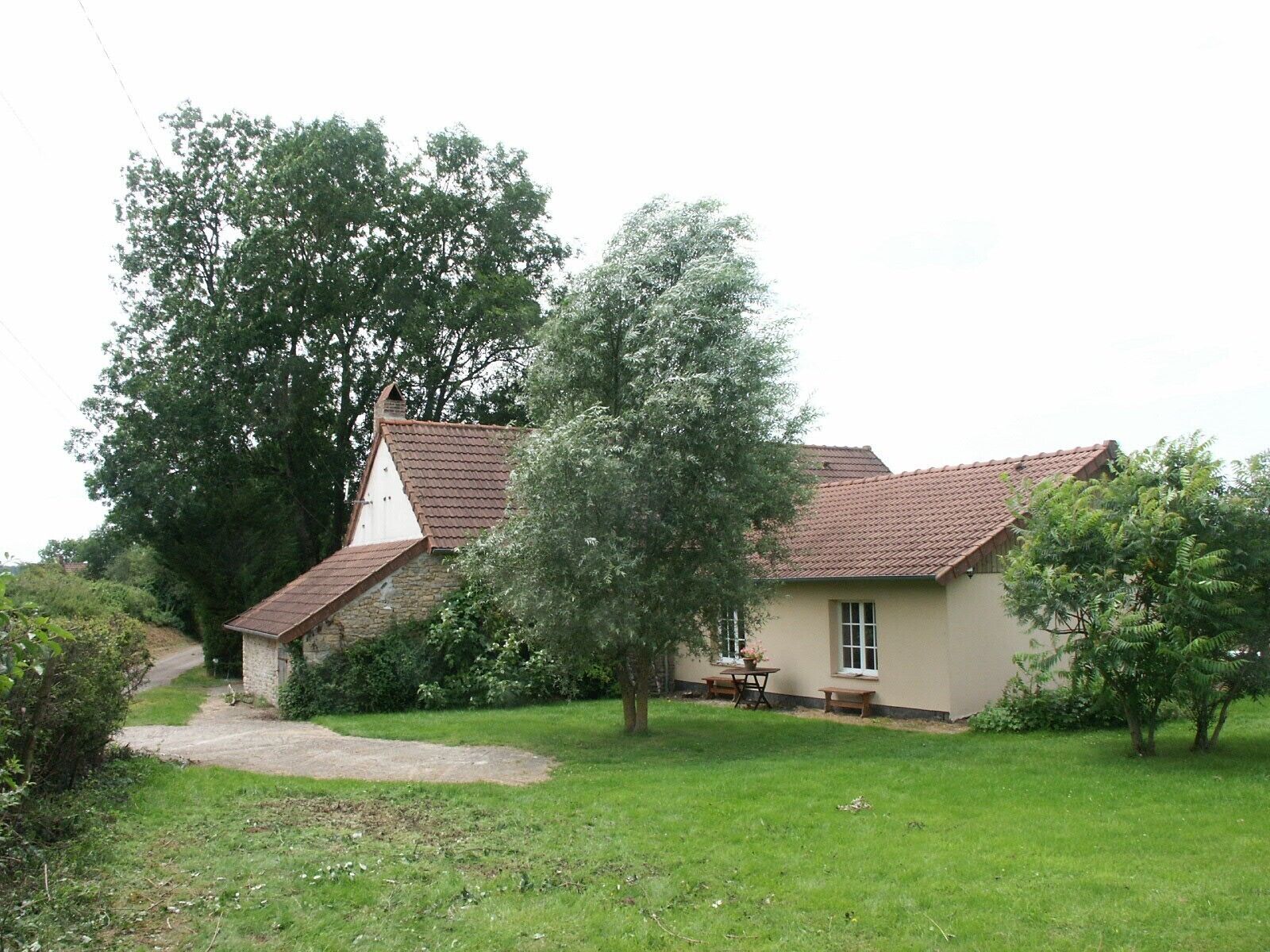 A house with a sloped roof, a visible chimney, and a small garden area with a pathway leading to the entrance.