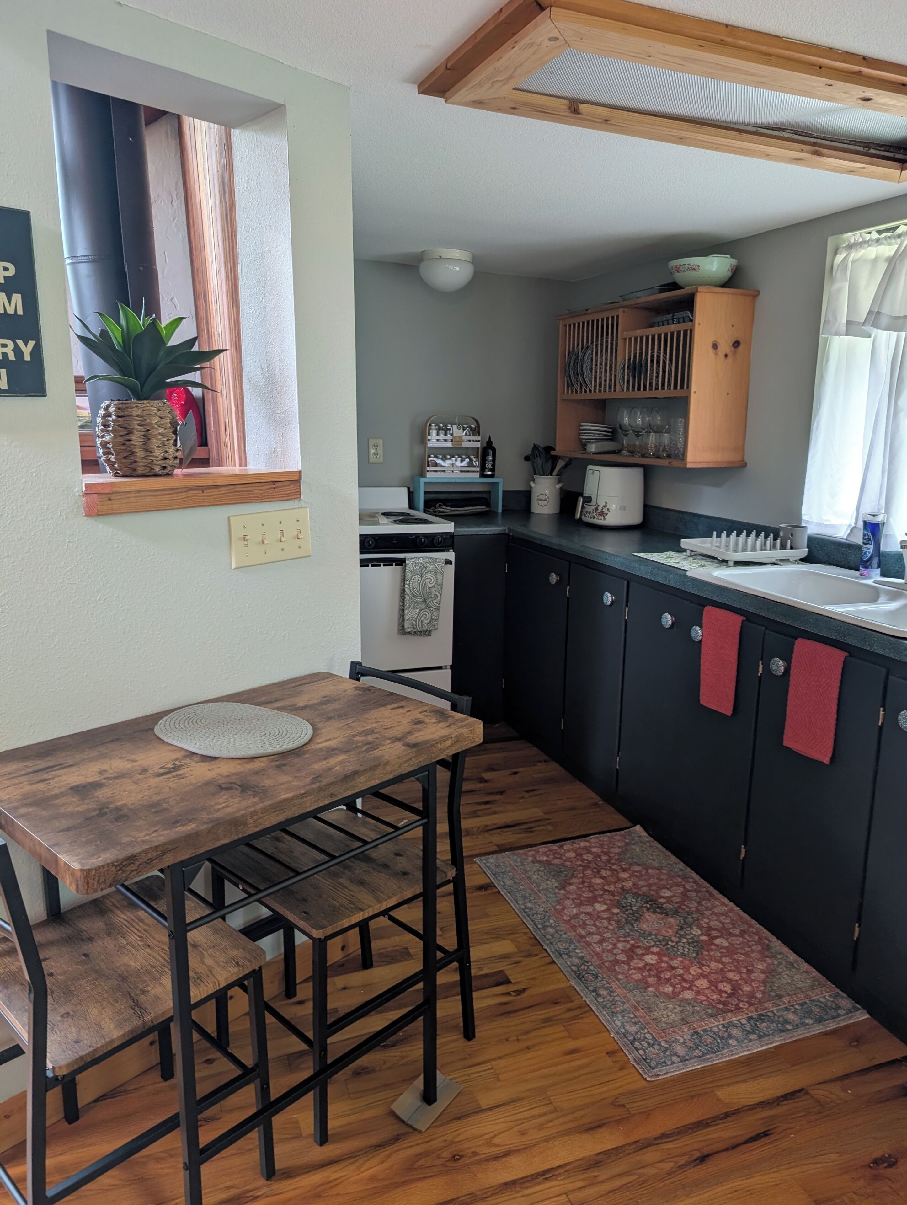 A compact kitchen with a wooden table, black cabinets, and a window with a plant.