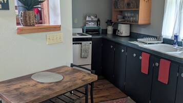 A compact kitchen with a wooden table, black cabinets, and a window with a plant.