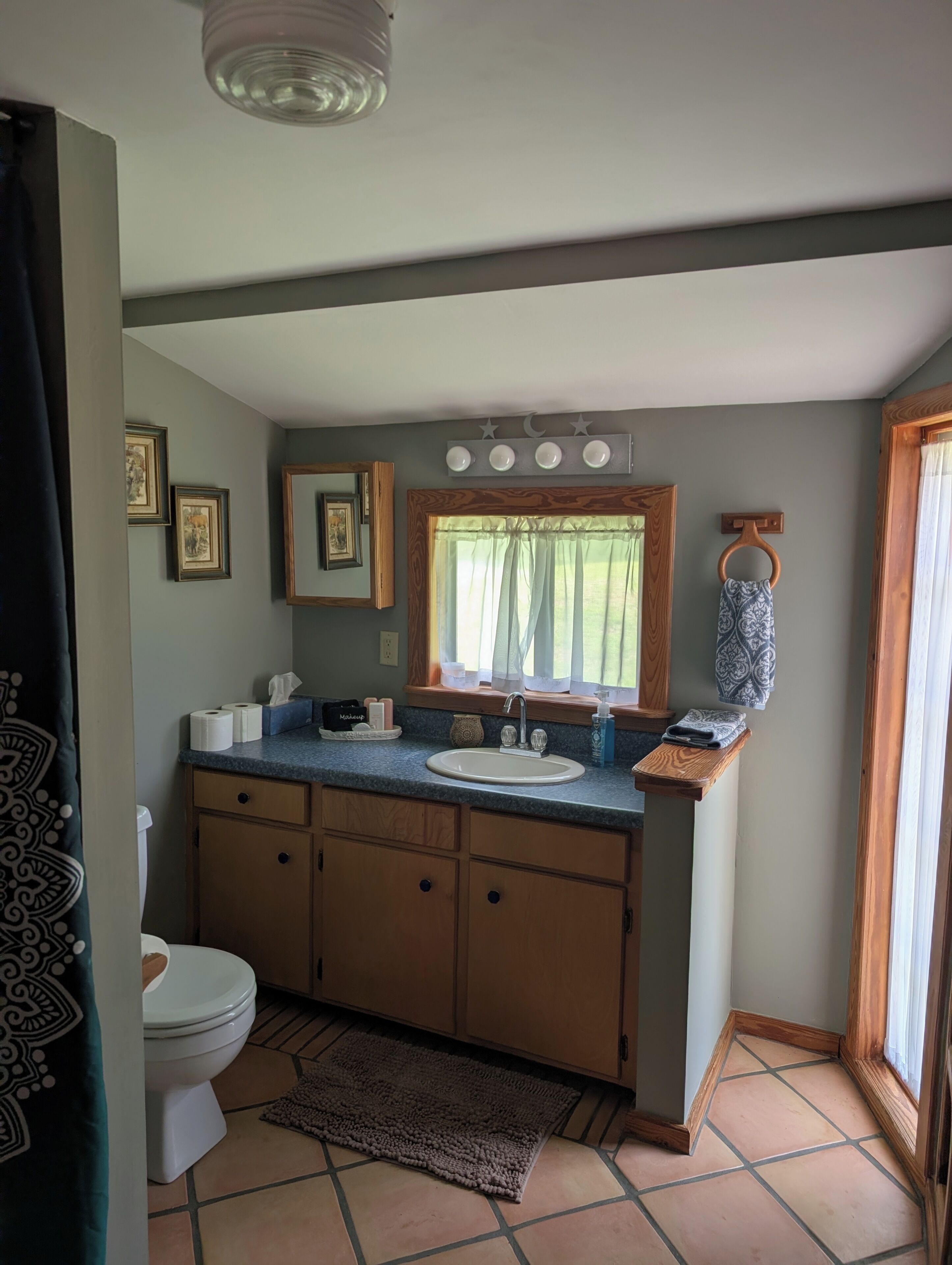Un baño con inodoro, lavamanos, tocador y una ventana con cortinas.