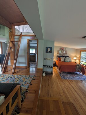 A room with a wooden ladder, a bed with a patterned bedspread, a bench, and a rug.