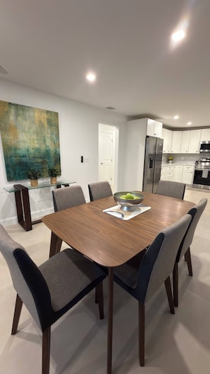 A modern dining area with a wooden table, six chairs, and a bowl of fruit.
