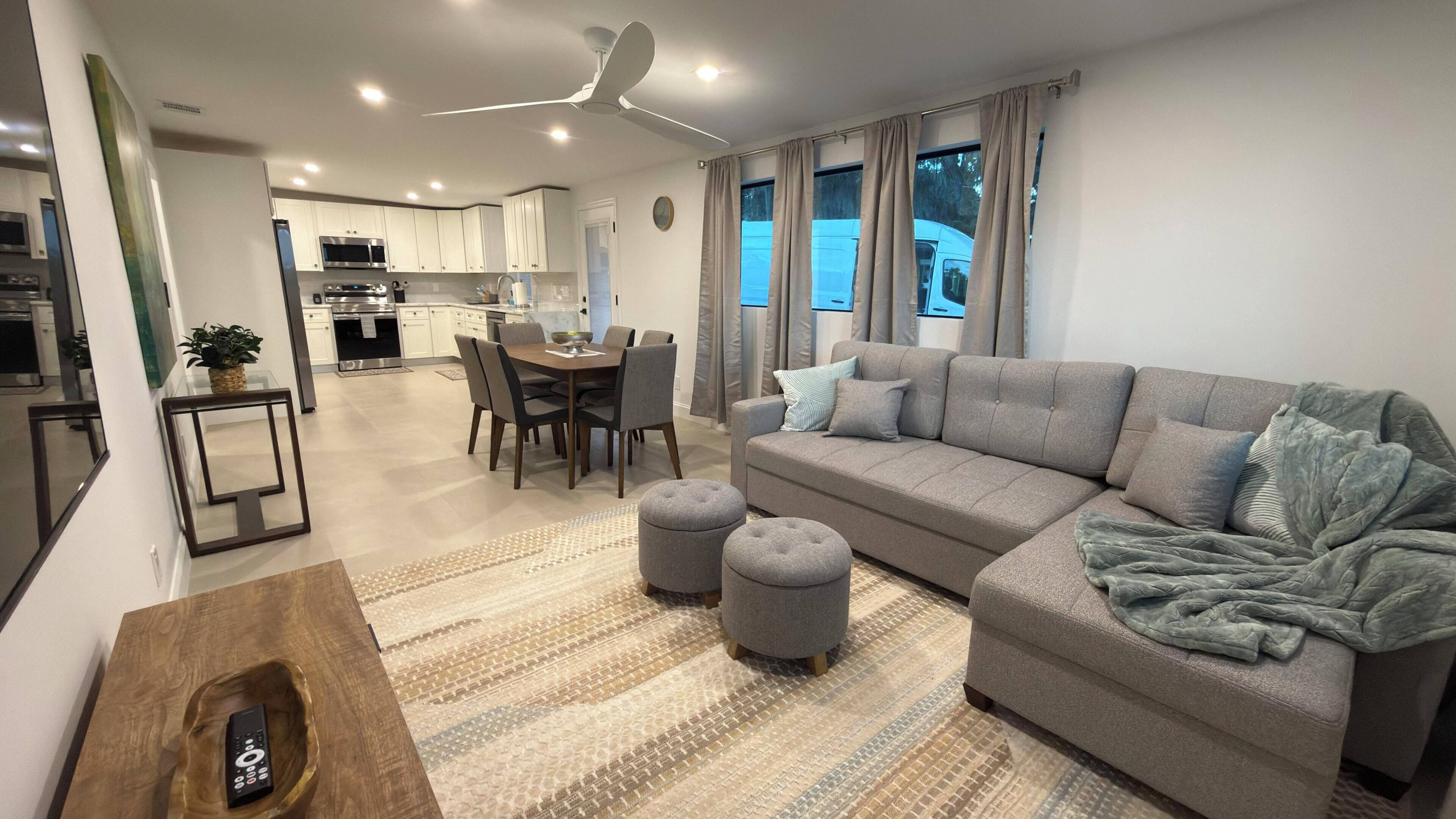 A modern living room with a grey sofa, ottomans, and a wooden side table with a remote control.