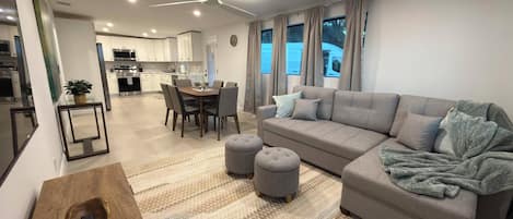 A modern living room with a grey sofa, ottomans, and a wooden side table with a remote control.