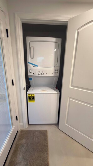 A laundry room with a front-loading washer and dryer, a door to the left, and a carpeted floor. - Beautiful 4-Bedroom Retreat in Sebring, Close to the Racetrack (Sebring)