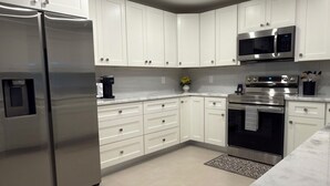 A modern kitchen with white cabinets, stainless steel appliances, and a marble countertop.