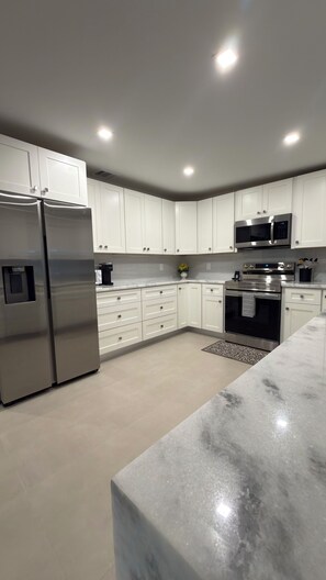 A modern kitchen with white cabinets, stainless steel appliances, and a marble countertop. - Beautiful 4-Bedroom Retreat in Sebring, Close to the Racetrack (Sebring)