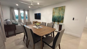 A modern dining area with a wooden table, six chairs, and a bowl of fruit.