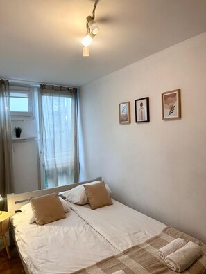 Ein Schlafzimmer mit einem Bett, einem Nachttisch, einer Lampe, einem Fenster mit Vorhängen und drei gerahmten Bildern an der Wand.