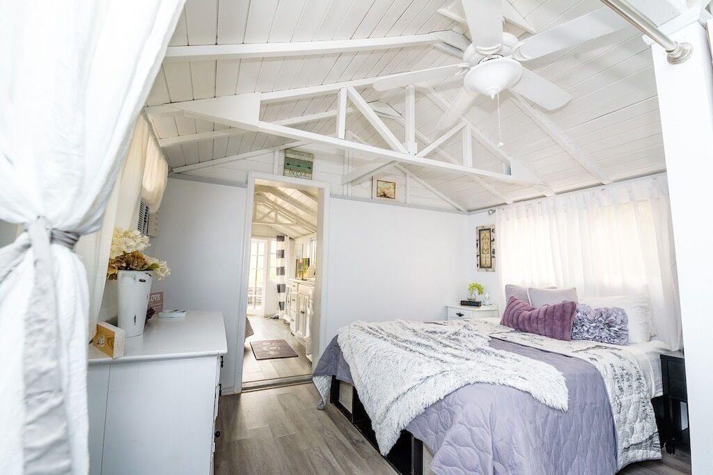 A bedroom with a bed, a desk, a chair, a ceiling fan, and a window with curtains.