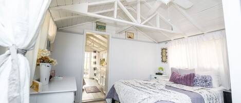 A bedroom with a bed, a desk, a chair, a ceiling fan, and a window with curtains.